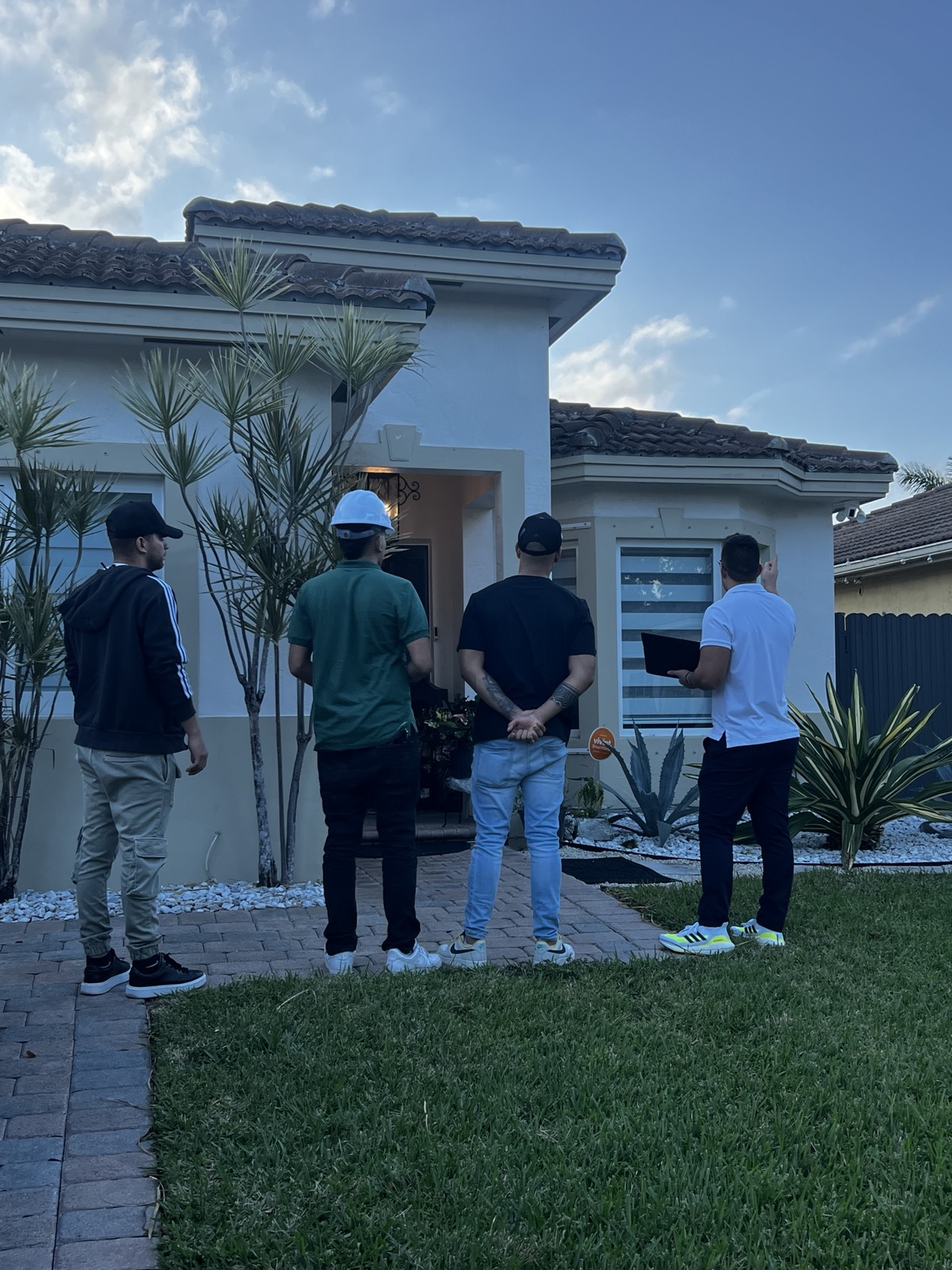 A Glowhaus setter team standing at a Miami home at dusk, one holding a tablet, during door-knock training.